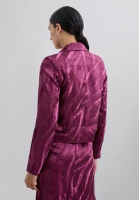 Chaqueta magenta con acabado satinado, que presenta un patrón de olas. El diseño incluye un cuello clásico y mangas ajustadas, cortada a la altura de la cintura.