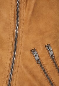 Tissu en daim tan avec trois zippers métalliques, un central et deux latéraux, dotés de tirettes rectangulaires et de surpiqûres contrastées. Texture lisse.