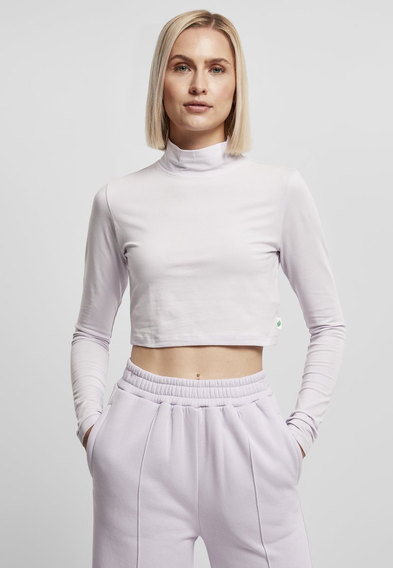 Lyselilla, langermet crop top med høy hals. Glatt, elastisk stoff og en liten grønn aksentlabel på siden.