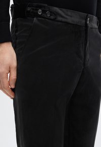 Schwarze Samthose mit schlankem Design, vorne mit Reißverschluss, zwei Knöpfen am Bund und glatter Textur.