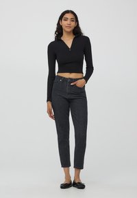 Top cropped a maniche lunghe rigate nera con mezza zip, abbinato a jeans grigio scuro a vita alta con cinque tasche e gamba dritta.