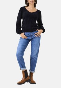 Schwarzer, strukturierter Pullover mit langen Ärmeln, kombiniert mit hellblauen Jeans mit aufgerollten Bündchen und braunen Stiefeletten mit schwarzen Akzenten.