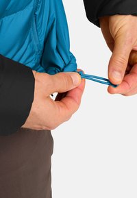 Tessuto di giacca blu con finitura testurizzata. Regolazione manuale del cordino elastico con cavo blu. Manica nera visibile, che mostra elementi a contrasto.