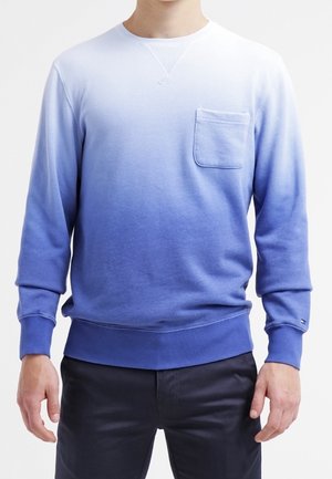 Hombre con un sudadera de manga larga en ombre que va del blanco en la parte superior al azul en la parte inferior, con un bolsillo en el pecho.