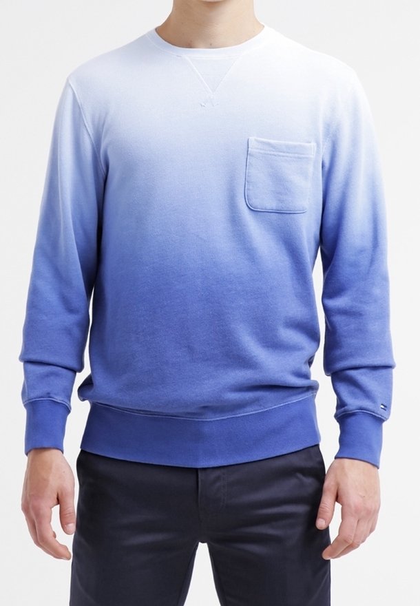 Hombre con un sudadera de manga larga en ombre que va del blanco en la parte superior al azul en la parte inferior, con un bolsillo en el pecho.