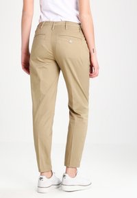 Khaki chino kalhoty s úzkým střihem, se zadními kapsami a knoflíkovým detailem. Nosič má na sobě bílé tenisky, což podtrhuje ležérní vzhled.