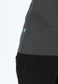 Grijs sportshirt met een blauwgele vlagdetail aan de zoom, gecombineerd met zwarte broek met een ritszak.
