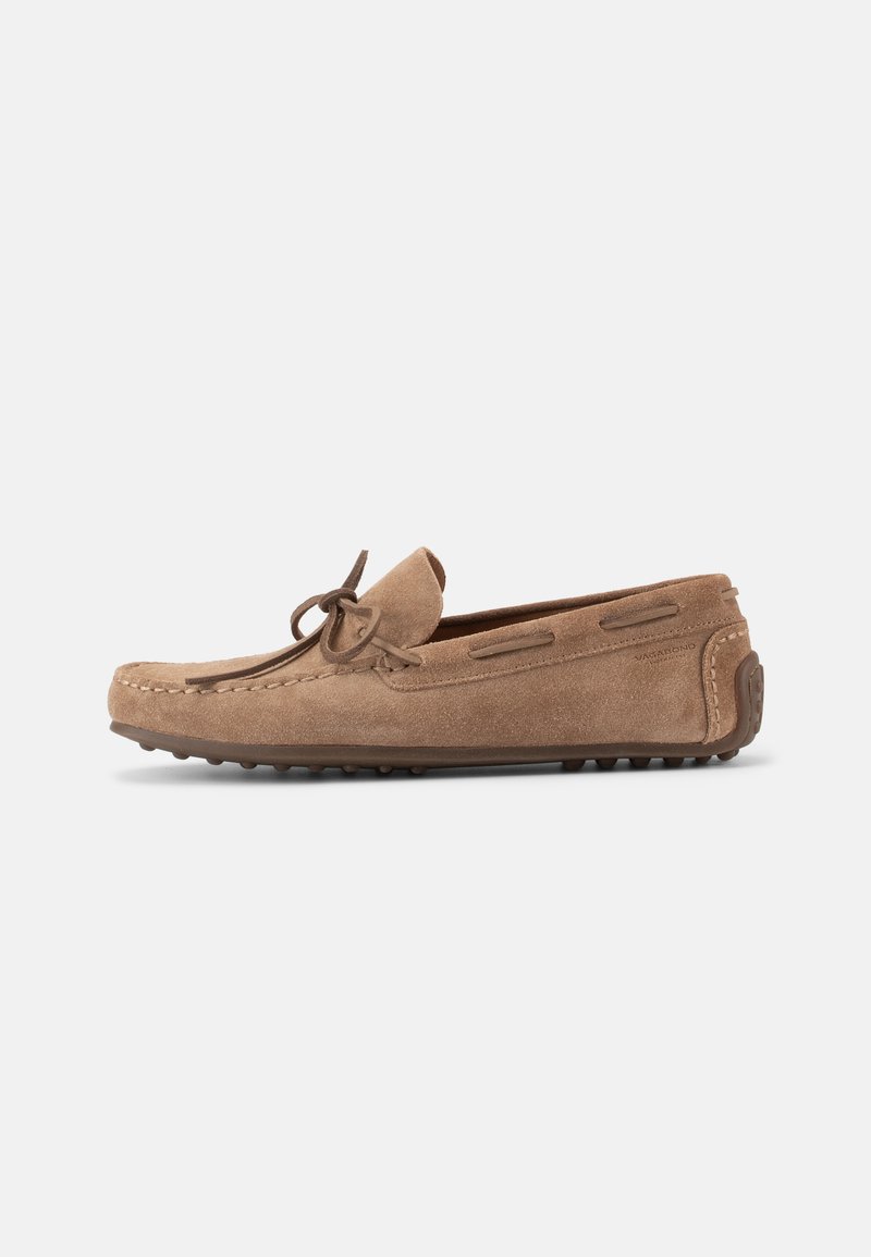 Lichtbruine suède rijloafer met strikdetail, mocassin-teenstiksel en rubberen steentjeszool, zijaanzicht tegen een witte achtergrond.