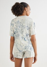 Kurzärmeliges, cremefarbenes Hemd und passende Shorts mit blauen himmlischen und botanischen Mustern. Weicher Stoff mit lockerer Passform und subtiler Textur.