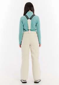 Beige sneeuwbroeken met verstelbare zwarte bretels, gecombineerd met een lichtblauwe fleece top. Gladde textuur, losse pasvorm, functioneel ontwerp.
