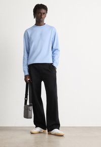 Sudadera azul claro con cuello redondo, pantalones negros, zapatos blancos y un pequeño bolso de hombro gris. El conjunto presenta un ajuste relajado.