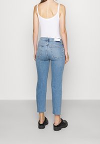 Jeans de mezclilla azul claro con cintura alta, corte ajustado, dobladillo sin terminar y dos bolsillos traseros. Combinados con una camiseta sin mangas blanca y zapatos de plataforma negros.