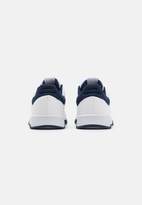 Chaussures de sport avec une base en cuir blanc et des accents en maille bleu marine, dotées d'un bout rond et d'une semelle blanche rembourrée. Deux languettes à l'arrière.