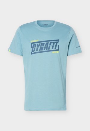 Svijetlo plava majica kratkih rukava s tamnoplavim logotipom "DYNAFIT" i malim žutim tekstom "SKIING EQUIPMENT" i "SINCE 1950" sprijeda.