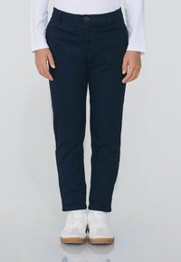 Granatowe spodnie wykonane z gładkiego materiału, o prostym kroju nogawek, z zapięciem na guzik z przodu i kieszeniami, zestawione z białymi trampkami.