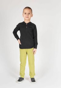 Czarna koszula henley z długim rękawem z drewnianymi guzikami, zestawiona z jaskrawozielonymi spodniami i czarnymi trampkami z białą podeszwą.