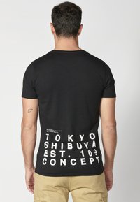 Juodas medvilninis marškinėliai trumpomis rankovėmis. Balti užrašai ant nugaros sako "TOKYO SHIBUYA EST. 109 CONCEPT", turintys geometrines erdves ir detales.