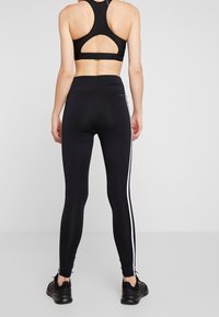 Leggings atléticos negros con rayas laterales blancas, diseño de cintura alta y material elástico. Combinados con un sujetador deportivo negro con un corte en la espalda.