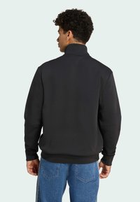 Sort zip-up sweatshirt med højt krave, der har en glat tekstur og ribbede manchetter. Bæres med blå denim jeans.