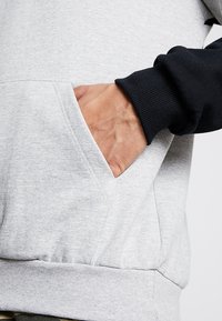 Felpa grigia e nera con tasca a marsupio. Presenta polsini e vita a costine. Realizzata in un tessuto morbido e texture.