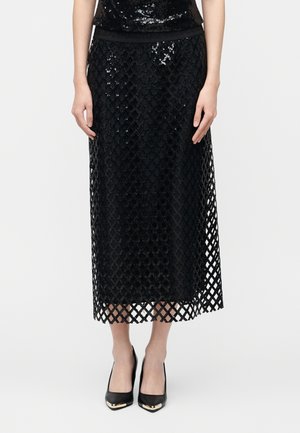 Fekete midi szoknya rácsos hálós réteggel és flitteres aljrészlettel, fekete, arany hegyű hegyesorrú magassarkúval viselve.