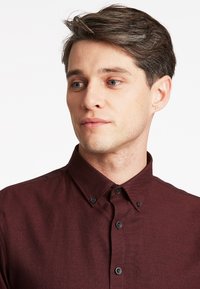 Bordeaux knoopshirt van een gestructureerde stof, met een puntige kraag en zwarte knopen, met een aansluitend ontwerp.