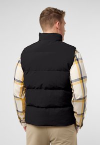 Schwarze Pufferweste mit hohem Kragen, ausgestattet mit glatter Textur und gestepptem Design, getragen über einem karierten Hemd in Gelb und Grau.
