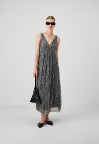 Robe maxi en tissu à motif noir et blanc, dotée d'un décolleté en V profond, d'un buste froncé et d'une silhouette fluide, accompagnée d'un sac à main noir.