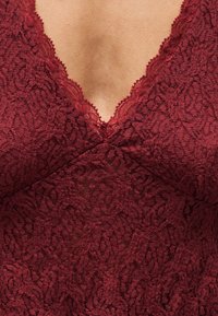 Gros plan sur un tissu en dentelle rouge foncé avec des motifs floraux et un décolleté en forme de V sur une peau claire.