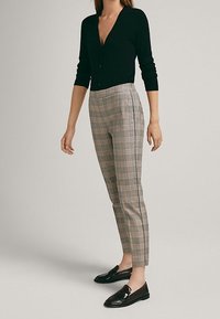 Cardigan noir à col en V et manches longues, associé à un pantalon à carreaux gris clair à coupe ajustée avec une bande latérale. Mocassins noirs.