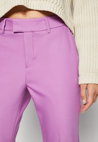 Pantalons lilas à la texture lisse, avec une taille plate, des passants de ceinture et des poches latérales, associés à un pull en tricot crème.
