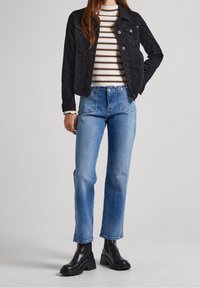 Svart denimjacka över en vit och randig topp, tillsammans med ljusblå raka jeans och svarta kraftiga klackboots.