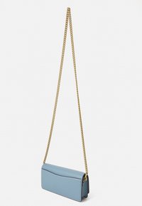 Lyseblå lærcrossbody-veske med en bølgete klaff, gullkjede-stropp og flat rektangulær form. Jevn tekstur med stitched detaljer.