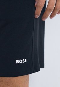 Svarte shorts laget av myk stoff, med en hvit logo "BOSS" nederst til venstre. Designet har en rett snitt og ingen synlige mønstre.