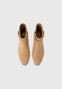 Bottines en daim beige avec une finition lisse, des pointes effilées et un détail de boucle sur le côté. L'intérieur est doublé de tissu doux.