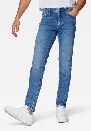 Jeans de denim azul con un corte slim, diseño de cinco bolsillos y un lavado desgastado. Usados con zapatillas blancas para un look informal.