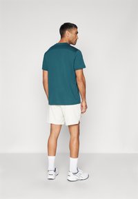 Türkise Kurzarm-T-Shirt, kombiniert mit weißen Shorts, getragen mit weißen Sneakers und weißen Socken. Glattes Material, lockere Passform und schlichtes Design.