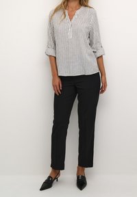 Blouse rayée blanche et marine avec un col en V et des manches trois-quarts, associée à un pantalon noir ajusté et des escarpins noirs pointus.