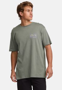 Olivenfarbener Baumwoll-T-Shirt mit kurzen Ärmeln, versehen mit einem bunten Berggrafik auf der linken Brust. Einfaches, lockeres Design.