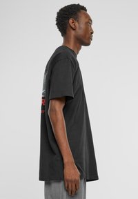 Sort bomulds T-shirt med en afslappet pasform, korte ærmer og et grafisk print på ryggen. Glat tekstur, rund halsudskæring og ingen synlige detaljer.