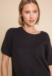 Kortermet svart genser i mykt, teksturert materiale med rund hals og avslappet passform, med en lett glans.