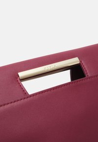 Sac Furla avec un design structuré en cuir bourgogne profond, présentant un accent en métal doré et des détails de couture contrastés.