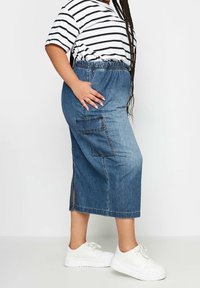 Falda midi de mezclilla con cinturilla elástica, aberturas laterales y un bolsillo de parche. Combinada con una camiseta a rayas y zapatillas blancas.