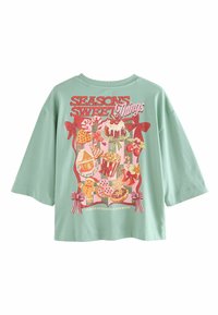Mint green oversized t-shirt featuring colorful graphic of sweets and treats. Text reads "SEASONS SWEET Things" with bows and festive designs.