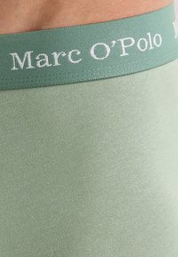 Ceinture élastique vert clair avec le logo "Marc O'Polo" en blanc. Tissu lisse et extensible avec un design sans couture pour un confort optimal.