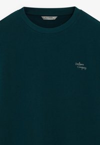 Mørk teal bomuld T-shirt med rund hals og korte ærmer, der har en lille hvid broderet logo på brystet.