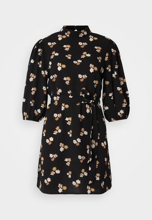 Melnās ziedu kleitā ir augsts dekoltē, pūkainas piedurknes, sasienams jostas siksniņa un baltiem un brūniem ziediem izšūta raksts.