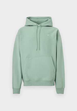 Világoszöld pulóver kapucnival, kenguruzsebbel, húzózsinórokkal és kis fehér Nike logóval a bal mellrészen, fehér háttér előtt.