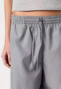 Grå trækknapshorts lavet af glat stof, med elastisk talje og sidesømme. Stoffet ser let og åndbart ud.