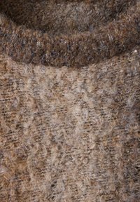 Gros plan sur un col de pull en maille épaisse et duveteuse et un tissu texturé dans des tons marron et beige.